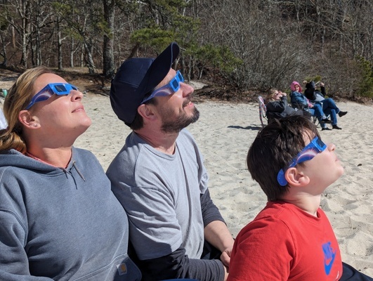 A group of fans gathered on a beach in Nickerson State Park in Brewster on Monday afternoon to watch the eclipse. Pictured here are, from left, are Kelly Kenna and Barry and Jack Semancik. ALAN POLLOCK PHOTO